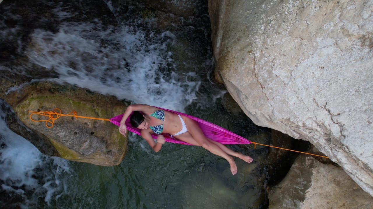 A traveller relaxing in a hammock strung above a freshwater wadi pool