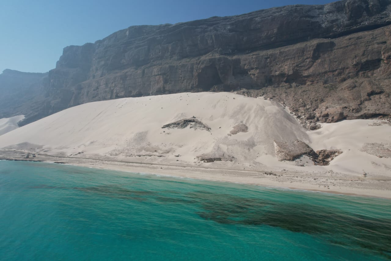 White dunes and turquoise sea below towering cliffs
