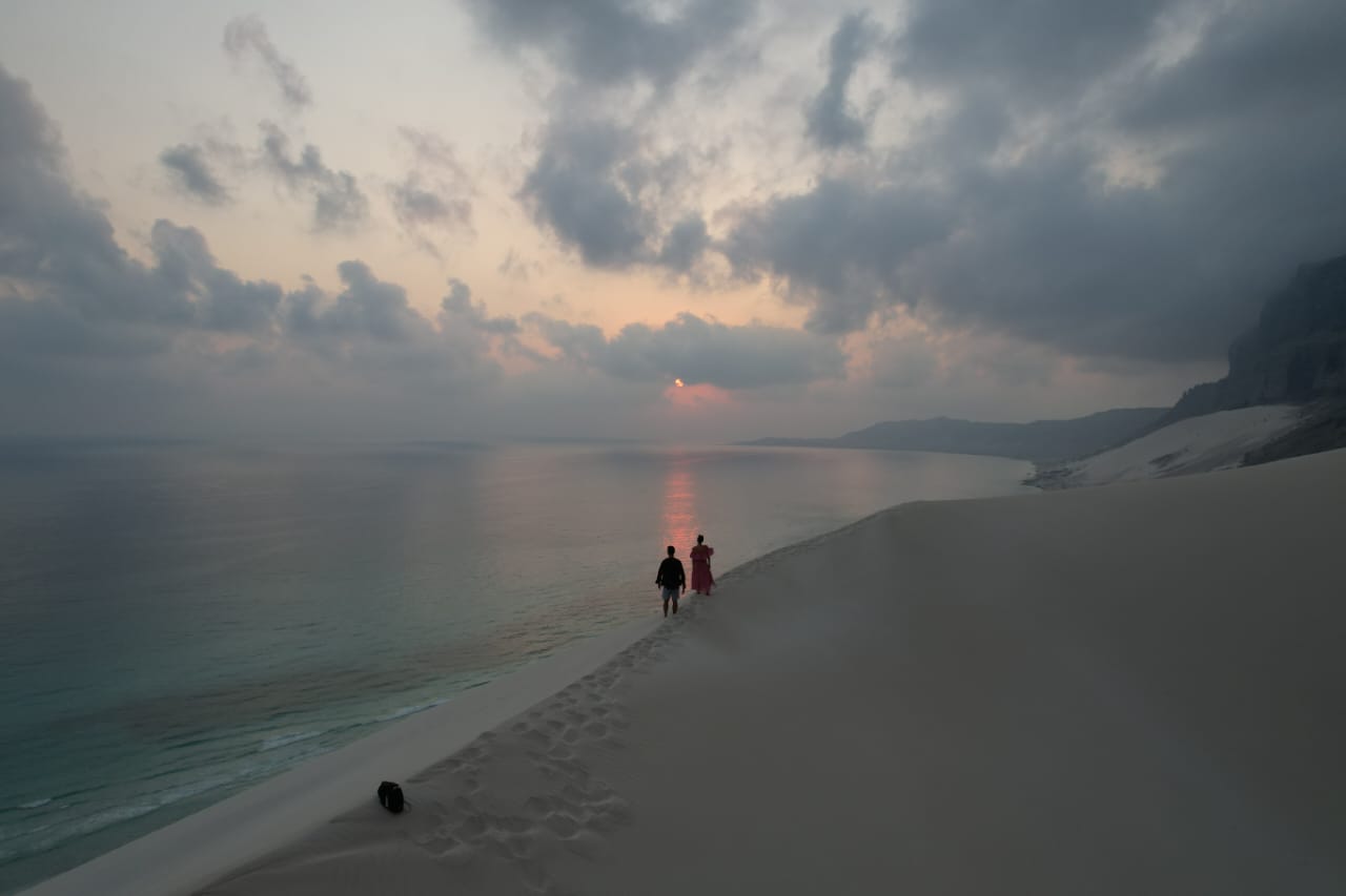 Two travellers walking a dune ridge at sunset